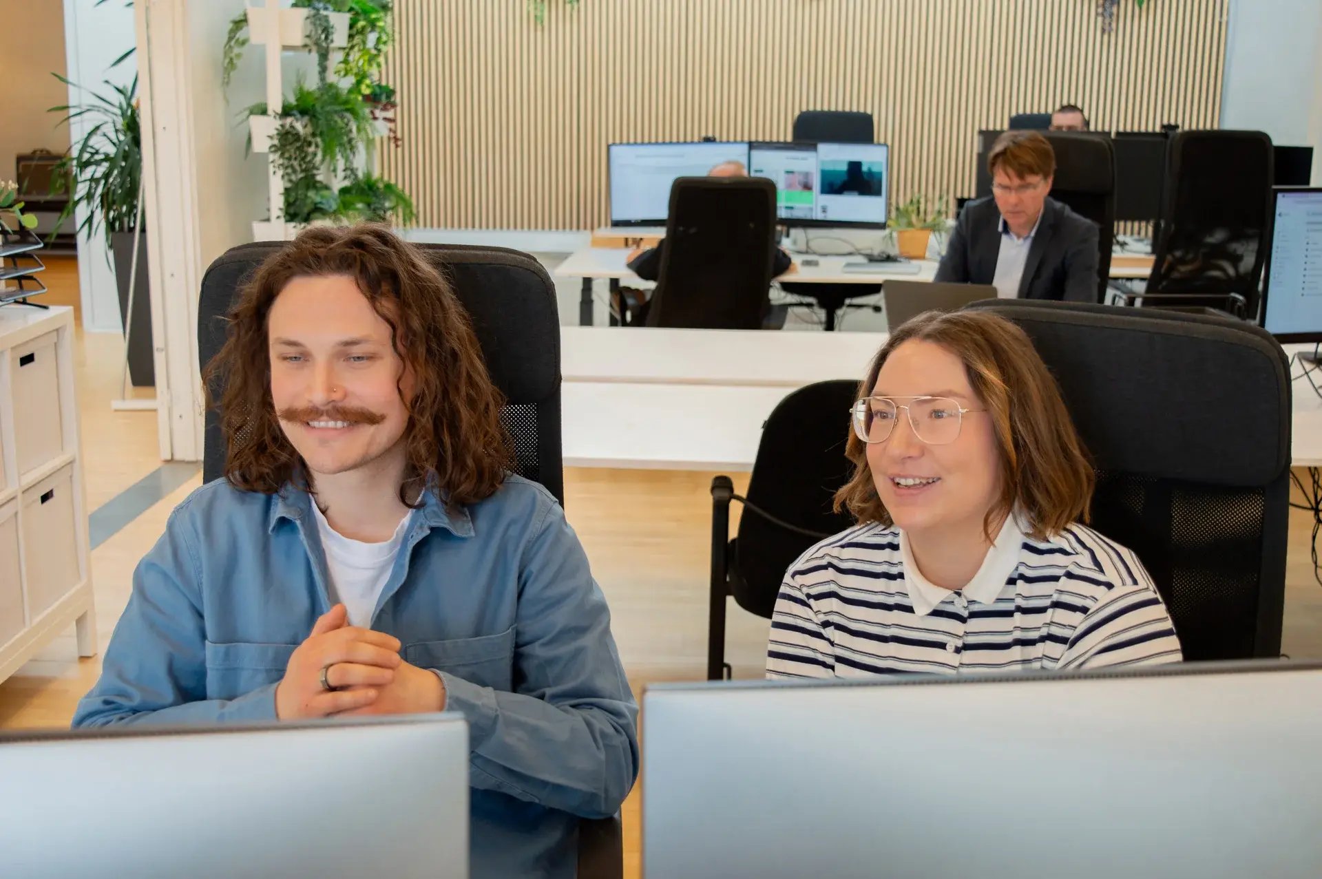 To kollegaer i et kontormiljø, der samarbejder foran en computerskærm